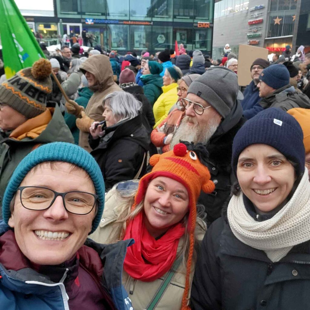 Sina und ihre Frau Jana auf einer Demo mit vielen anderen Menschen. Dieses Bild symbolisiert das Thema Gemeinsamkeit.